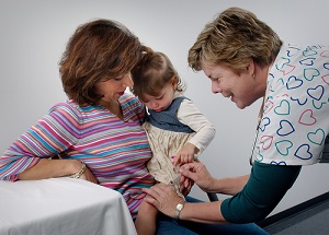 child being held by a woman while getting her injections from a nurse