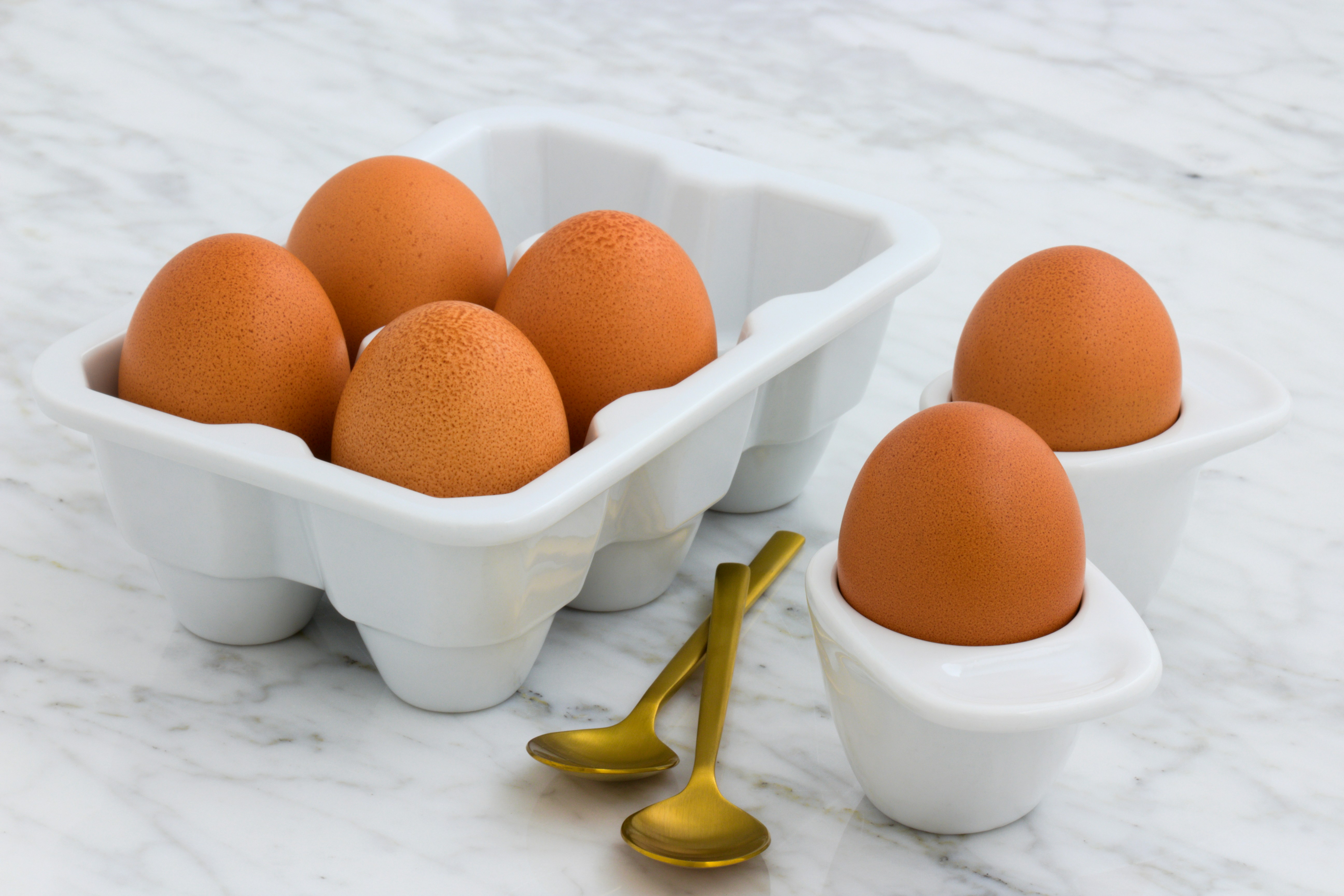 4 eggs in a an egg carton, 2 eggs in egg cups with two gold coloured spoons on the marble counter.