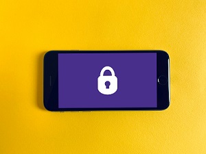 smartphone sits on a yellow background. Displayed on the phone screen is a white padlock against a purple background.