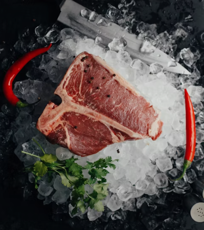 a raw steak on a bed of ice, framed by two red chilli peppers, a parsley garnish and a silver knife